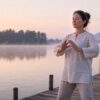 Woman practicing calm Qigong at dawn on a lakeside dock