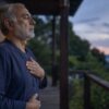 Older man practicing deep diaphragmatic breathing on a porch at dusk