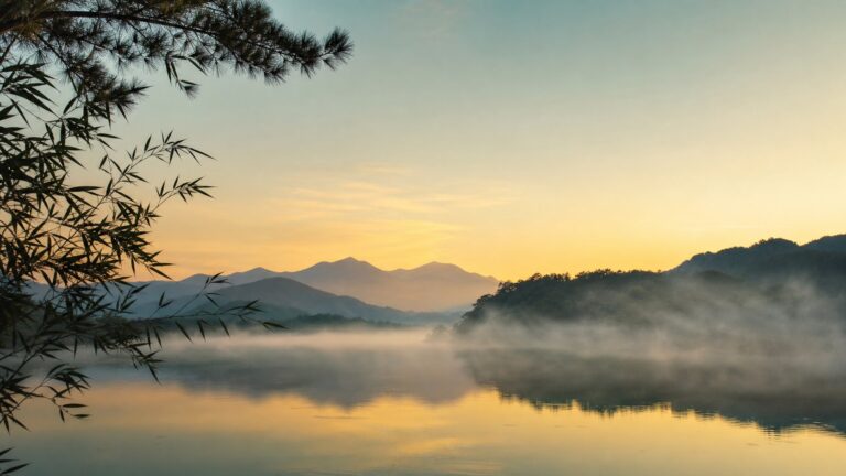Mist drifting in slow horizontal bands over a still lake at dawn, bamboo and pine silhouetted at the edge
